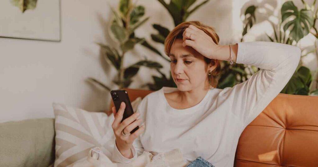 Woman on a sofa reading her phone with a worried expression, considering an unsolicited publishing offer